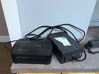 Photo showing two APC power backup units placed side by side on a table, with power cords visible.