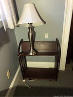 Photo showing Levenger bookcase with dark wood finish on castors, holding the lamp, against a wall.