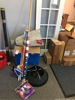 Wide shot showing various items including rolls of wrapping paper, beach umbrella, flag, black plastic Christmas tree stand, and packaged knitting loom