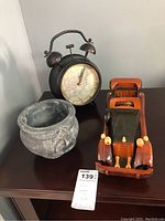 Photo showing the clock, stone vase, and wooden model car on a dark wood table