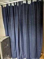 Photo of two dark blue curtain panels hanging from a rod in front of a cabinet.