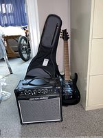 Full view of Mitchell black electric guitar with Road Runner guitar case and Acoustic amplifier.