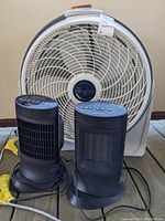Front view of two Honeywell ceramic heaters and a Lasko Cyclone box fan, showing control panels, cords, and fan grille.