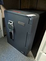 Angled front view of the gray safe showing electronic keypad, handle and logo