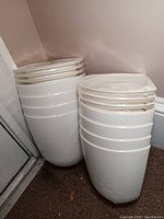 Stacked white plastic corner wall mount flower pots sealed in original wrapping, showing their curved shape and flat backs.