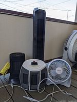Photo showing two space heaters: a black Honeywell HCE309B and a white and black Pelonis HC-014Ah ceramic heater. Also includes a white Honeywell fan and a tall black Holmes Tower fan.