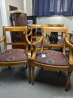 Frontal view showing all four wooden arm chairs with moon and star pattern fabric seats. Chairs are placed close together inside a room with a window and curtain in background.