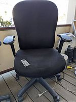 Front view of black Tempurpedic office chair with fabric upholstery, armrests, and caster wheels. Visible wear on seat and backrest.