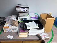Overall view of the lot showing spiral notebooks stacked, multiple boxes of Quality Park envelopes, black desk organizer tray, and two bags of elastic bands.