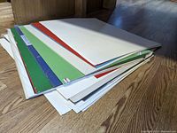 Stack of poster boards on hardwood floor showing multiple colors and unopened packaging