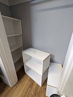 Seven white stackable storage shelves placed together in a corner showing their size and condition.