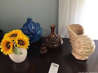 Overview of all items including white vase with sunflowers, blue vase, amber glass bottle with stoppers, ammonite-shaped vase on table.