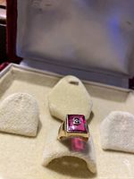 Ring displayed front-on in beige velvet display pad inside red velvet ring box showing top view.