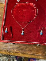 Full set displaying necklace with pearl pendant and matching earrings on red velvet backing