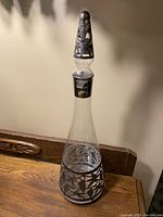 Full view of the antique cut crystal decanter with silver overlay and stopper on a wooden surface.