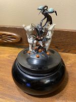 Overall view of the antique trinket box showing round dark wooden base and lid decorated with silver bird, turquoise stones, coral beads and cream-colored figurines.