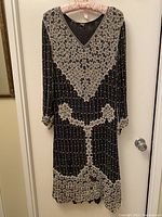 Front view of black silk dress with extensive white beading in floral and grid-like patterns, showing overall design and dress shape.