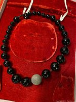 Image showing full view of black onyx bead necklace with large silver round bead against red velvet case interior.