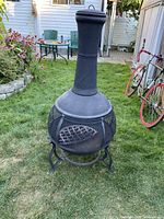Front angled view of black cast iron chiminea on grass with mesh sides and tall chimney pipe.