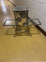Three-quarter angle view of the glass and metal three-shelf stand showing circular decorative metal side panel and glass shelves.