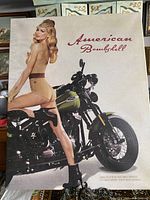 Framed American Bombshell poster showing a woman on Harley Davidson motorcycle, prominently displaying title and artwork.