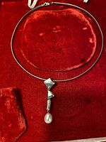 Full view of silver choker necklace with tear drop pearl pendant on red velvet background.