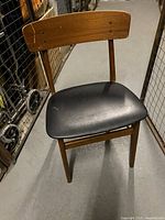 Front angle view showing wood frame and black upholstered seat with a small rip.