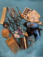 Overview of the mixed lot items including the electric drill, scissors, combs, metal coasters, small metal cup, plastic decorative stones, and fish-shaped bottle opener.