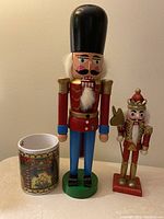 Two hand-painted nutcracker figurines and holiday mug with fireplace scene shown together