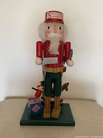 Front view of the hand painted wooden nutcracker figure standing on a green base along with a toy block and small figurine attached at the base.