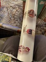 Photo showing a close-up section of the wallpaper roll with detailed Christmas ornaments including red Christmas baubles and nutcracker figures on a white background.