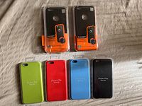 Top view showing two Spigen cases in original packaging and four Apple silicone cases out of packaging in green, red (Product), blue, and black.