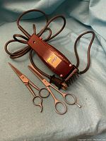 Oster hair clipper with attached power cord and two pairs of scissors lying on a blue cloth.