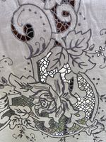 Close-up photo showing detailed gray embroidery with floral and leaf patterns and crocheted lace inserts in the tablecloth fabric.