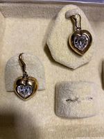 Front view of two heart-shaped earrings with gold washed silver and clear heart-shaped stones upright on jewel display stand