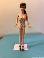 Front view of vintage Barbie doll wearing original striped bathing suit and black high heel shoes, displayed on a stand.