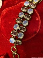 Close-up photo of bracelet featuring two rows of cushion-cut semi precious stones set in metal frames on a red velvet background.