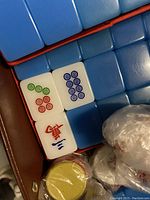 Close-up photo showing white Mahjong tiles with blue, red, and green symbols, and the blue backs of tiles.