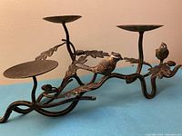 Side angled view of the metal candelabra with three candle plates, one bird perched on branch and detailed leaf and acorn decorations.