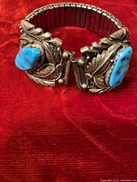 Photo of the stretchable Navajo sterling silver watchband highlighting the large turquoise stones and detailed leaf designs on a red fabric background.