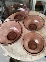 Group shot of all four purple nesting Pyrex bowls arranged on a marble table, largest bowl at back, bowls nested and spaced around.