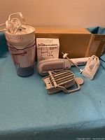 Vintage Donvier Shakemaker motor top with clear plastic mixing cup and accompanying Steambuddy steamer parts, instruction manuals laid out on blue cloth.