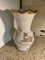 Full view of vintage textured ceramic vase with deer design and gold flared rim on a countertop.