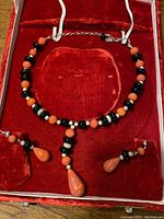 Necklace and earrings set with orange and black beads alongside silver beads arranged in a red velvet display case.