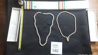 Two pearl necklaces laid flat with a measuring tape and a jewelry box visible.