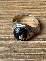 Close-up photo of gold-tone men's ring with small diamond and black onyx showing front and side band detail.