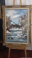 Full view of framed oil painting showing snowy landscape with river and trees under cloudy sky