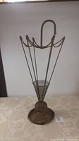 Front view of metal wire umbrella stand shaped like an umbrella with hoop handle and round base.