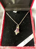 Red jewelry box with black interior holding the necklace with amethyst pendant and a label indicating '14K GOLD GEMS STONE'.