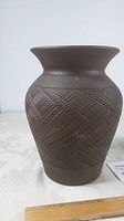 Side view of the brown pottery vase showing detailed carved geometric patterns and flared rim.